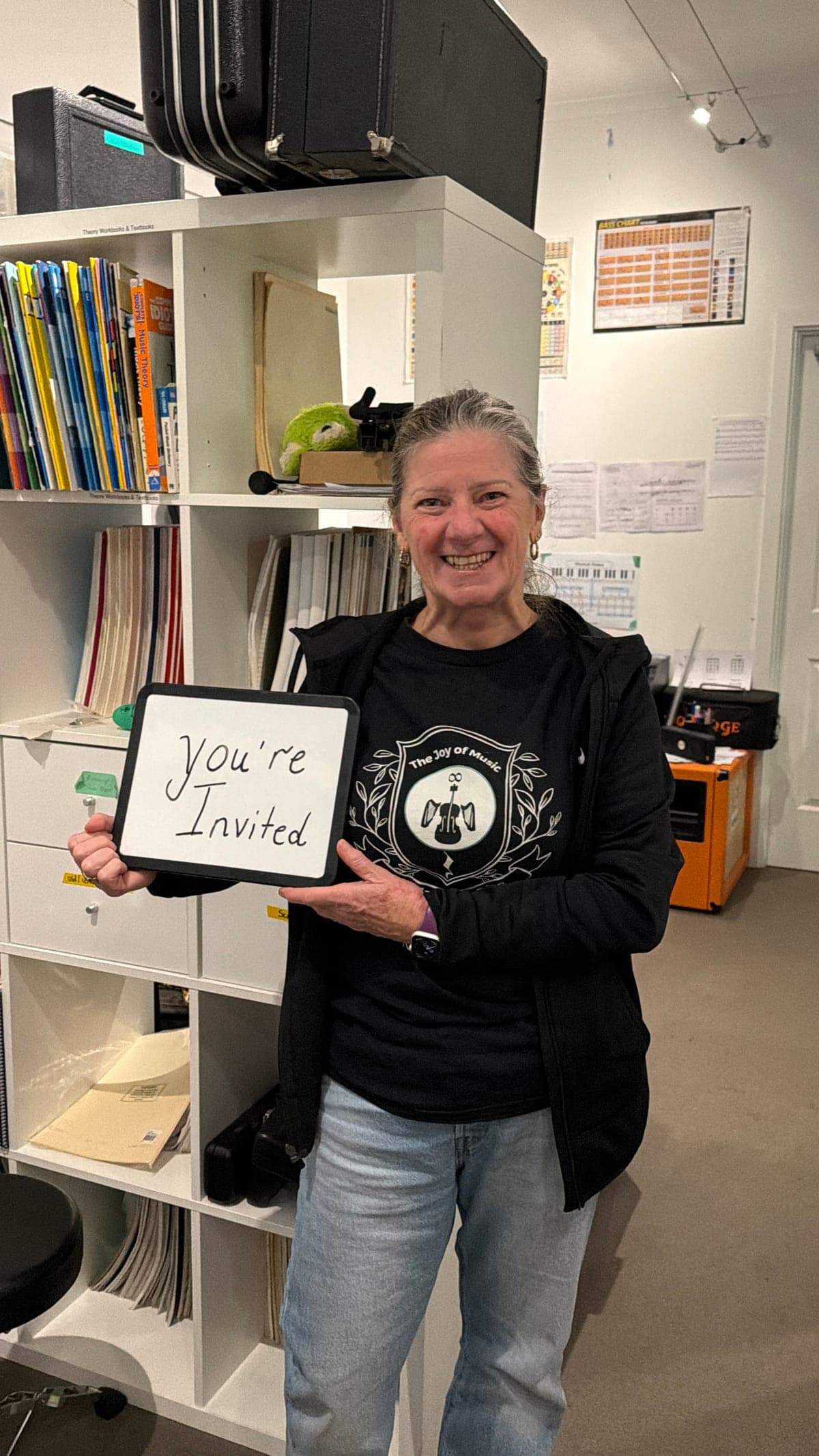 A Music Eternal teacher in the Seacliff studio holding a whiteboard reading: You're invited