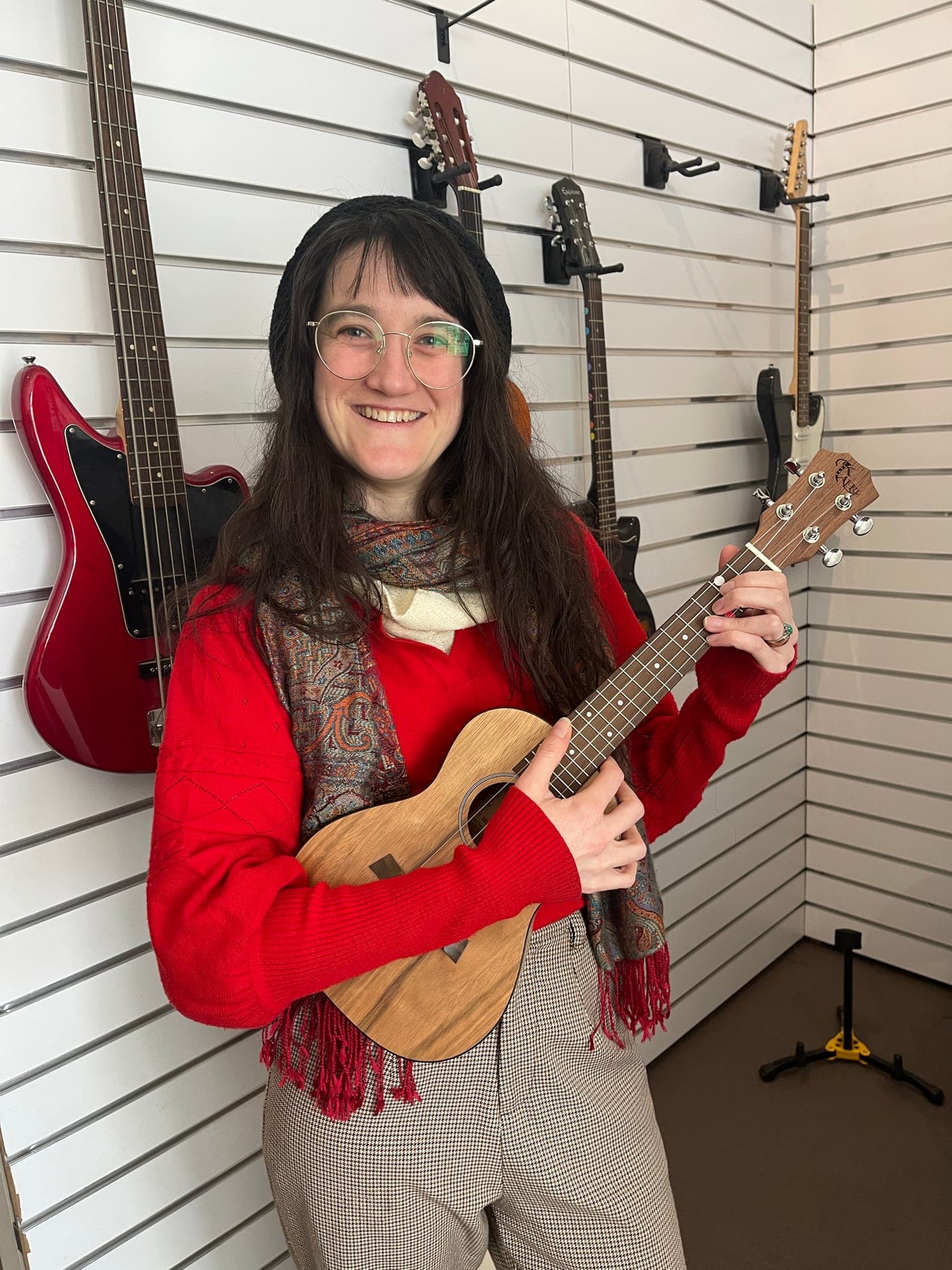 A woman playing a ukulele in front of the guitar wall at the Music Eternal studio